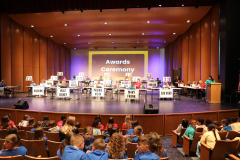 Stage set up for an event, with a group of people seated at tables in front of a stage and podiums, with a sign that reads
