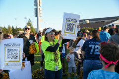 Woman holding sign at outdoor event, surrounded by people and signs.