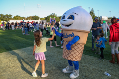 Mascot in ice cream costume standing next to child, both waving at camera at event.