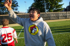 Boy in a red and white jersey standing on a field, waving his hand.