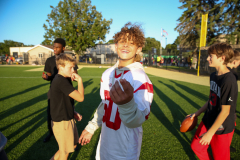 Young man in football uniform holding up peace sign, standing on field surrounded by other players.