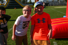 Two young boys posing together at an event, one wearing glasses and a green shirt, both smiling and looking at the camera.