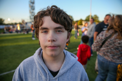 Boy in a grey hoodie standing on a grassy field during an event.