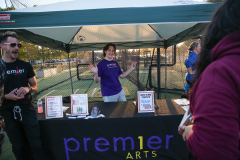 People standing around a tent at an outdoor event, with one person inside the tent holding a sign that says "premier arts".