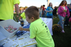 Child in yellow shirt reaching into container of candy at table.