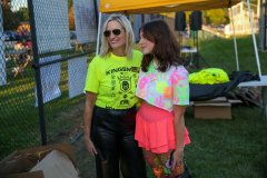 Two women standing in front of a tent at an event, one wearing a colorful outfit and the other in black pants and a yellow