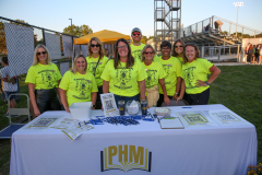 Team of people in front of a table at an event, all wearing shirts with the same logo and message.