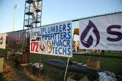 Signs on fence advertising local businesses at outdoor event.