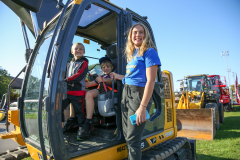 Woman sitting in a yellow construction vehicle with two children.