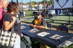 Man in yellow jersey at baseball game signing autographs for fans.
