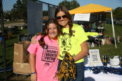 Woman in yellow shirt standing next to table with items on it.