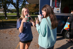 Two girls standing outside a food truck, enjoying their drinks and snacks.