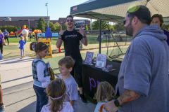 Man in black shirt standing behind table at outdoor event, smiling at camera.