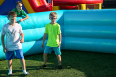 Three children standing in front of inflatable bounce house at an outdoor event.