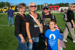 Four women posing together at a football game, smiling and looking towards the camera.