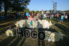 People gathered at a park for a Penn State HOCO event, celebrating homecoming with a sign that reads "Penn State HOCO" and a