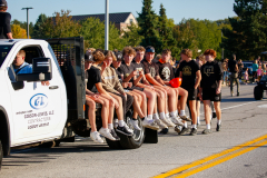 People sitting on a truck bed during a parade.