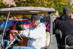Older man driving golf cart in parade.