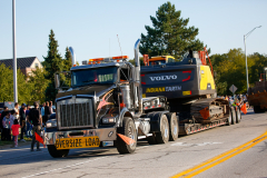 Large truck pulling a trailer carrying a smaller truck on a flatbed.