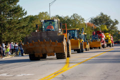 Parade float on roadway featuring large construction vehicles.