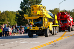 Large yellow truck driving down a street during a parade.