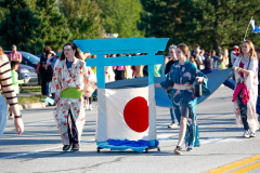 People in colorful costumes walking down a street at an event.