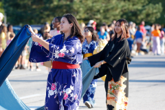 Two people in traditional japanese attire holding blue fabric during a parade.