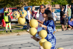 Woman in blue dress holding yellow balloons at parade.