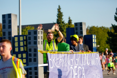 Two people waving from a parade float that reads "breaking ground for deaf children" and has blue blocks on either side.