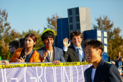 This is a photograph of a group of people standing in front of a large cardboard cutout of a building, which appears to be a