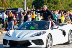 Man in convertible sports car waving to crowd at parade.