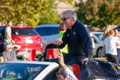 Man standing on car hood in parade, waving to crowd.