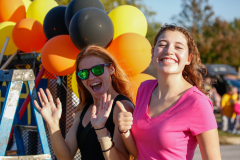 Two women posing in front of a balloon arch at a parade.