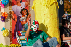 Man in a wrestling mask sitting on a float at a parade.