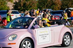 Pink Volkswagen Beetle convertible in a parade, with people inside and around it, celebrating Hoco Parade.