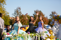 Three women in princess dresses on a float at a parade.