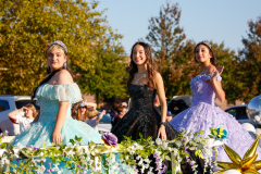 Three girls in princess costumes standing on a float during a parade.