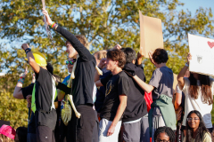 People at a protest holding signs, one person taking a selfie with the crowd in background.