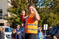 Man in orange vest standing next to baby.