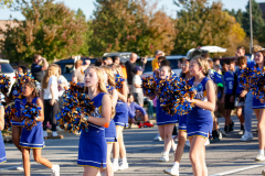 Group of cheerleaders in uniforms holding pom poms, standing on a street during a parade.