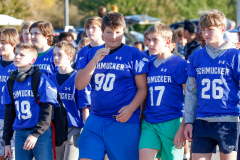 Teenagers in blue football uniforms walking together down a street during a parade.