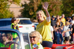 Woman in yellow shirt waving from back of red car during parade.