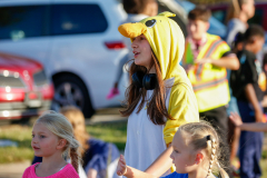 Girl in yellow animal costume at parade, smiling and waving to crowd.
