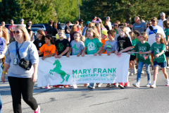 Children in sports uniforms holding a banner at an event.