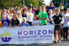 Children participating in a parade, walking together on a street.