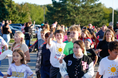 Children participating in a parade, walking together down a street.