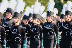 Marching band members in uniforms, standing together in a line.