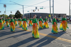 Group of people in colorful costumes, dancing on a city street during a parade.