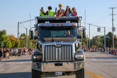 People riding in back of a large truck during a parade.
