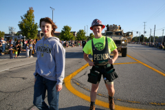 Two people standing on a street, one wearing a hat and the other a vest, both looking towards the camera.